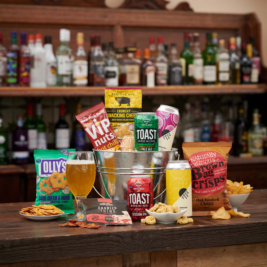 The Beer Bucket gift hamper including beers from Toast and Full Circle Brew Co. set out on a table top in a bar in front of a range of spirits and alcoholic beverages.