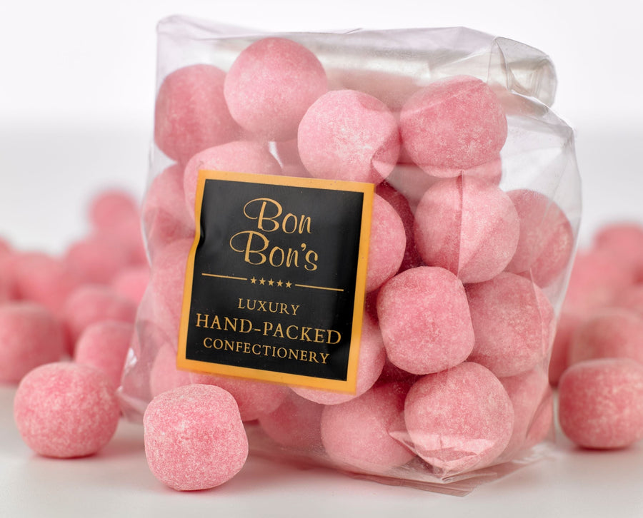Strawberry bon bons from the confectionary maker, Bon Bon's. Their luxury hand-packed confectionary has been opened with bon bons spilled across the table. 